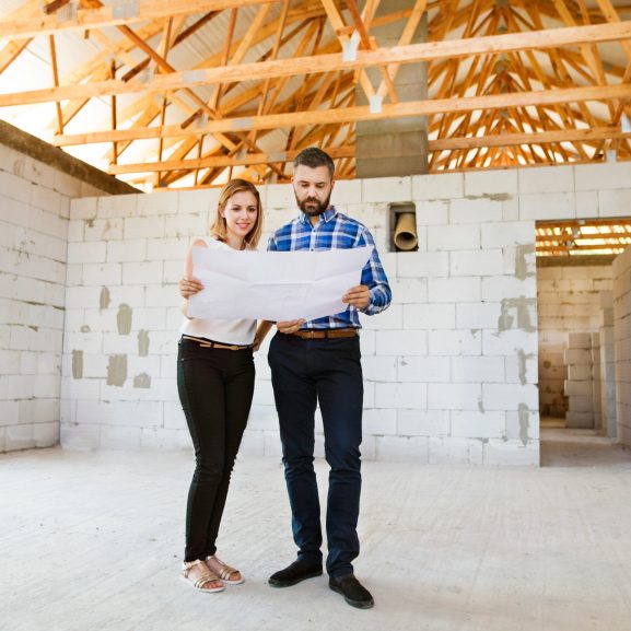 Young couple or architects or civil engineers looking at plans of the new house, discussing issues at the construction site.